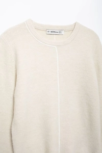 Close-up of cream knit sweater neckline with contrast trim and brand size label