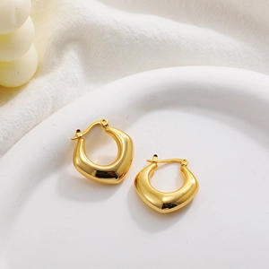 Close-up of chunky gold hollow U-shaped hoop earrings on a minimalist white ceramic tray