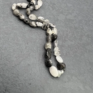 Close-up of natural black rutilated quartz necklace with irregular beads on stone background