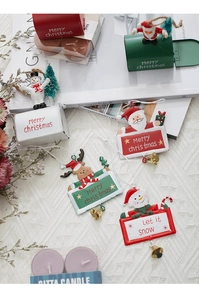 Detail of Christmas iron mailbox and Santa tags on white knit texture with a scented candle