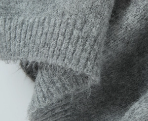 Detailed macro view of the soft grey knit texture and elastic ribbed cuff of the sweater