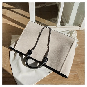 Detail of a large canvas tote bag featuring black leather trim and elegant metal chain strap