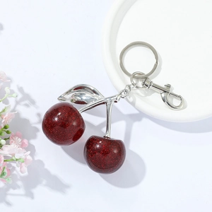 Sparkly red cherry keychain with silver leaves and lobster clasp on white dish