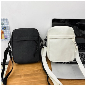 Close-up of black and white canvas crossbody bags showing front zipper pocket and strap
