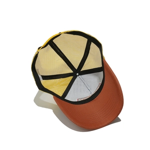 Detail view of yellow and rust red trucker hat showing breathable mesh and inner structure
