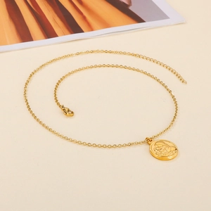Vintage gold-plated stainless steel necklace with a circular embossed coin pendant on a beige surface
