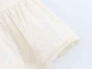 Détail du chemisier blanc avec tissu texturé en losange et broderie de dentelle fine