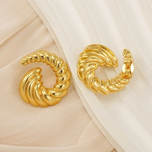 Gros plan détaillé de boucles d'oreilles torsadées dorées sur tissu texturé doux