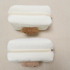 Detail of white quilted plush pouch with brown bear embroidery and metal zipper closure