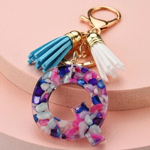 Macro shot of resin letter Q keychain with colorful stones and blue white tassels