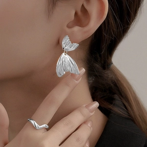 Gros plan sur des boucles d'oreilles queue de poisson et une bague vague en argent poli