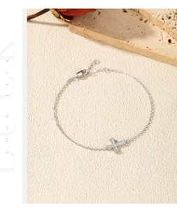 Close-up of S925 silver cross bracelet with Moissanite stones on textured beige surface