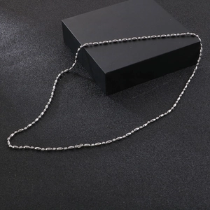Macro detail of silver stainless steel bead chain necklace on a minimalist black surface