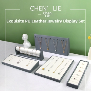 Gray PU leather jewelry display set with necklace stands and ring trays on white fabric
