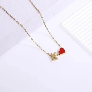 Detail of gold chain necklace with red heart and K letter pendants on white stand