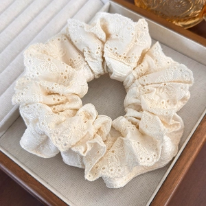Detailed view of beige fabric scrunchie featuring delicate embroidered lace texture