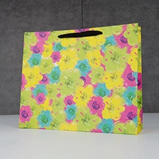 Close-up of a white paper gift bag featuring vibrant floral patterns and black handle cutout