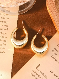 Close-up of golden C-shaped acrylic earrings with metallic finish on vintage background