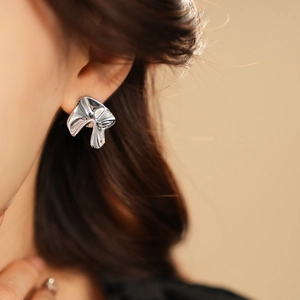Close-up of silver irregular geometric metal stud earrings worn by a model in soft light