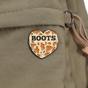 Detail shot of heart-shaped leopard print brooch with Boots text on olive canvas