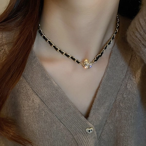 Détail de la chaîne dorée avec cordon en cuir noir et pendentif boule pavée de diamants