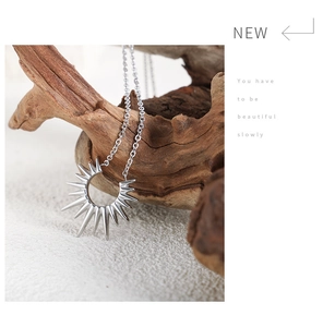Close-up of starburst pendant necklace hanging on driftwood with a minimalist white background