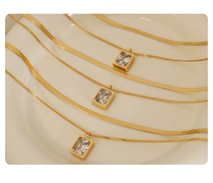 Close-up of three gold blade chains with rectangular zircon pendants on white ceramic