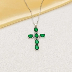 Detail of cross pendant necklace with green oval zircons and shimmering white gems