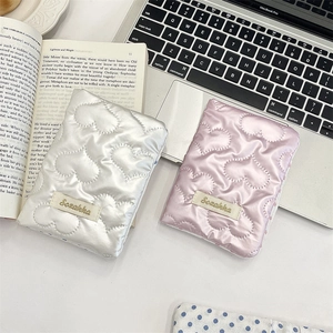 Pink and silver heart-quilted travel organizers shown on a desk with a laptop and books