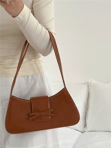Detail of brown glossy leather underarm bag featuring a stylish bow on the front flap