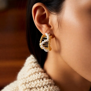 Detailed view of C-shaped gold pearl earrings worn with a beige knitted sweater