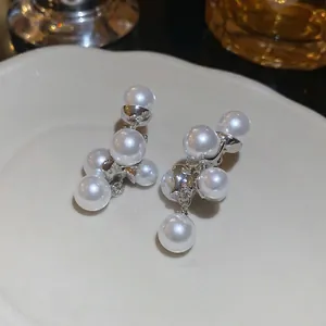 Eleganti orecchini pendenti con perle argentate esposti su un piatto di ceramica