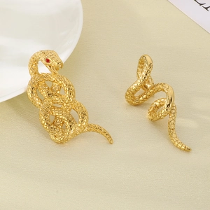 Detailed view of 18k gold plated snake earrings with small red crystal eyes on beige surface
