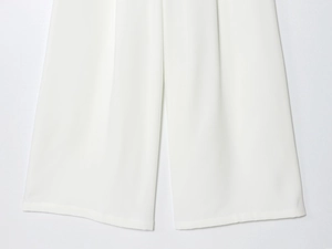 Détail du pantalon large blanc montrant les coutures de l'ourlet et le drapé du tissu