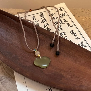 Close-up of green jade cloud pendant with hand-woven brown rope on wooden tray