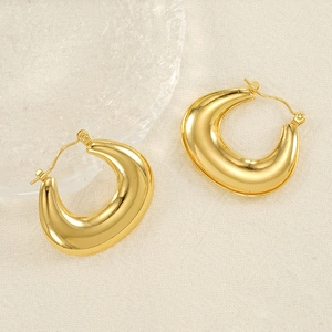 Detail of chunky gold U-shaped earrings with a polished mirror finish on fabric