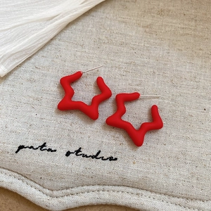 Detail showing matte red star-shaped acrylic earring on a textured linen background