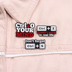 Macro shot of three creative Ctrl shortcut enamel pins on pink denim fabric material