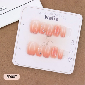 Faux ongles faits main dégradé pêche avec perles et pointes pailletées sur carte de présentation