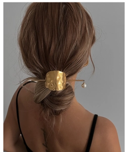 Detail view of a gold metallic hair stick with irregular texture and pearl pendant