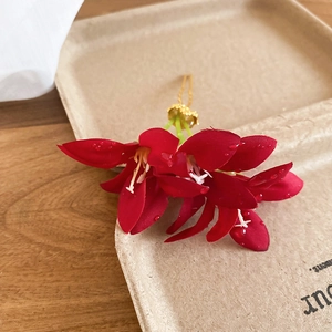 Detail view of handmade red fabric flower hairpin with golden base on paper tray