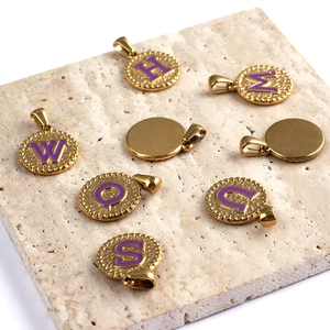 Macro view of gold stainless steel pendants with purple enamel letters on stone surface