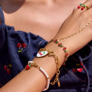 Detail of red cherry pendant jewelry set with gold bracelets and white pearls on wrist