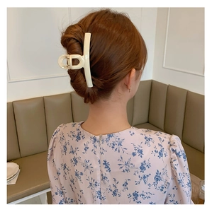 Detail of cream white hair claw clip featuring a CD letter design on a bun hairstyle