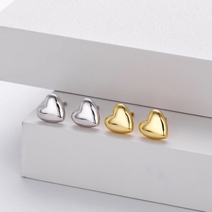 Polished silver and gold 3D heart stud earrings on a geometric display stand