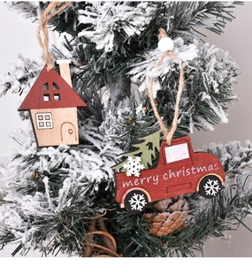 Detail of wooden Christmas ornaments featuring a red truck and cabin hanging on a snowy tree