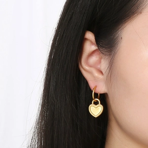 Close-up of gold heart lock earrings with beaded edges and brushed metal texture