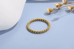 Detailed view of a gold minimalist twisted rope ring on a textured fabric backdrop