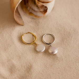Close-up of gold and silver pearl drop earrings on a natural beach shell background