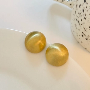 Detail of matte brushed gold dome stud earrings on a white minimalist ceramic plate